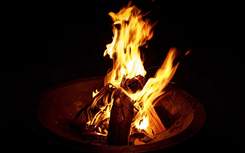 Wood fire burning in a bowl-style fire pit with visible embers and firewood Wood fire burning in a bowl-style fire pit with visible embers and firewood