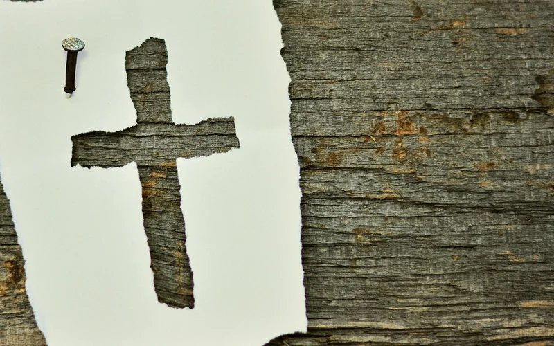 Cross shape cut from paper revealing natural wood grain underneath