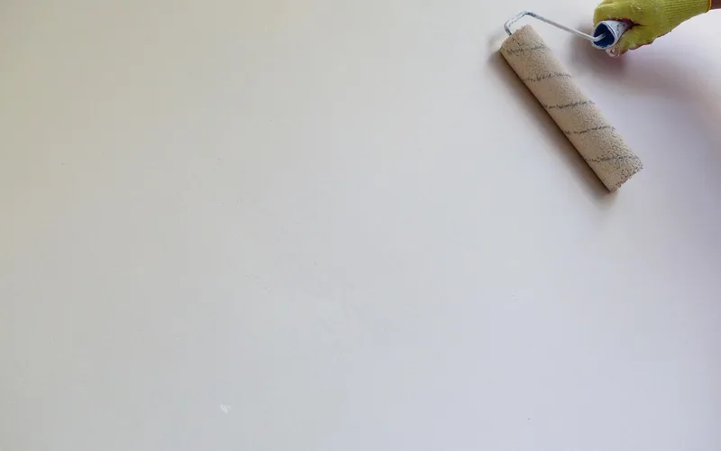 gloved hand using a paint roller to apply an even coat on a white wall