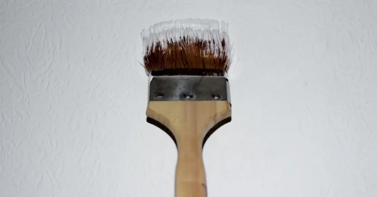 paintbrush loaded with white paint touching up a textured interior wall