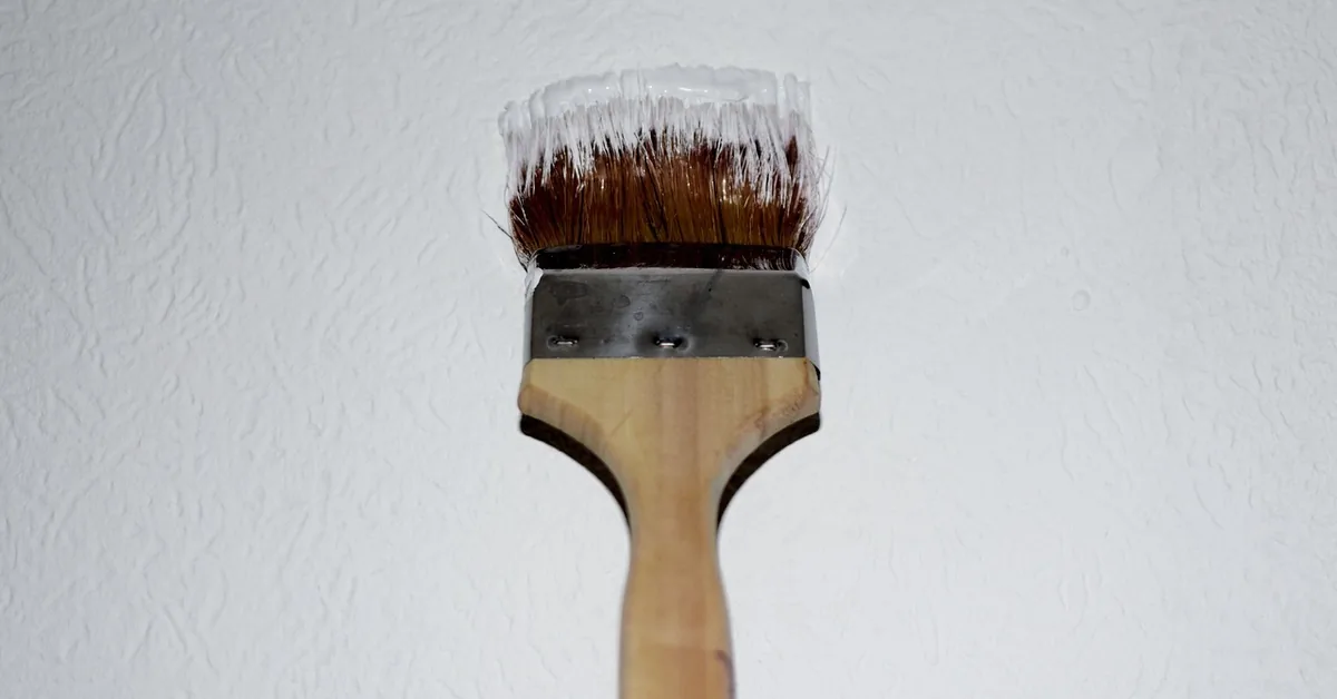 paintbrush loaded with white paint touching up a textured interior wall