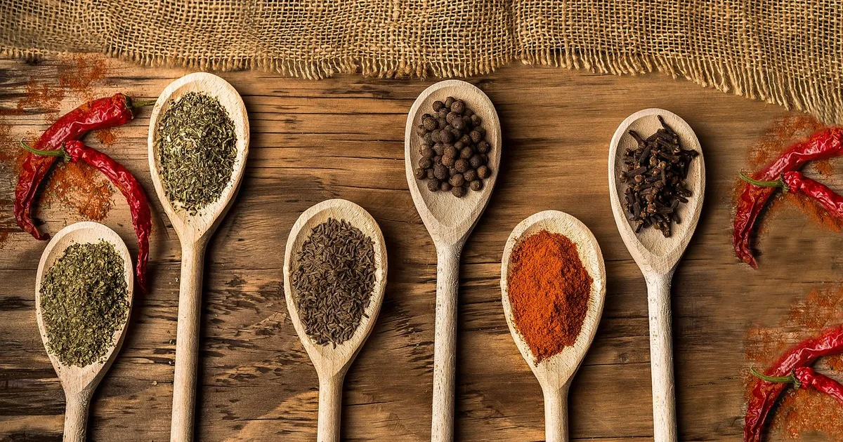 Wooden cooking spoons filled with spices on a rustic wooden table