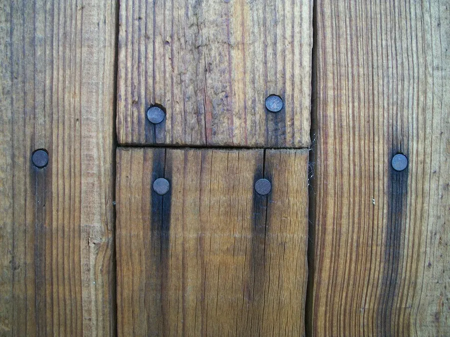 Dark black streaks running down from steel nail heads in old wood floor boards