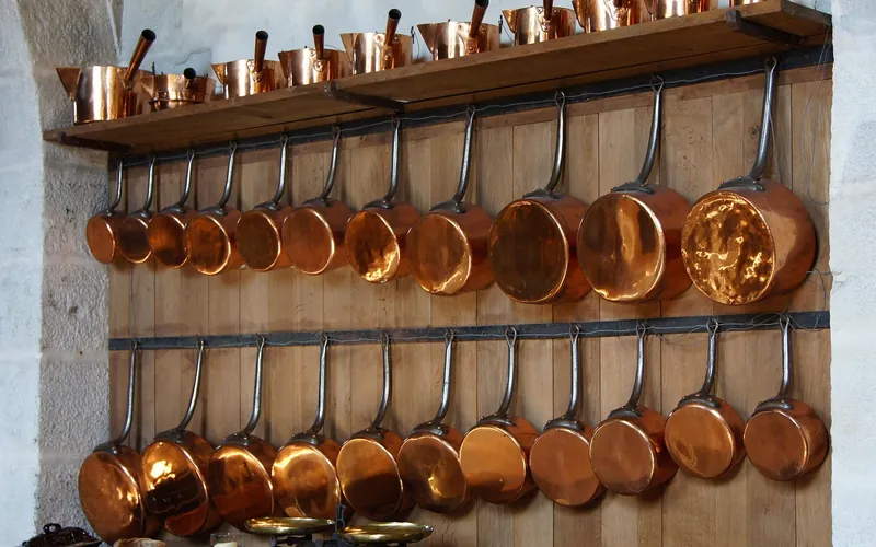 Copper saucepans with long metal handles hanging on a wooden wall rack