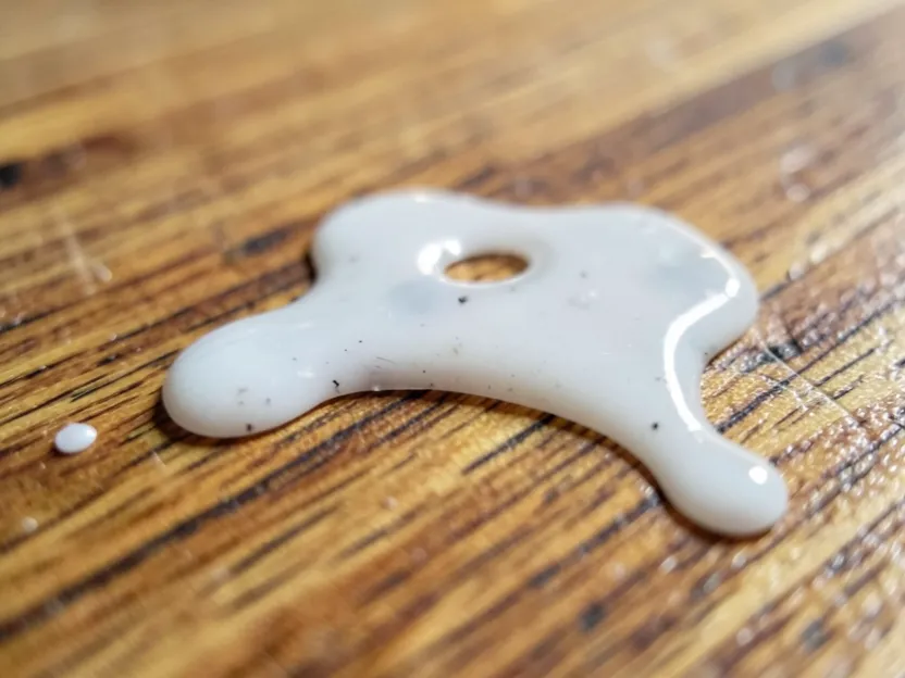 Dried super glue drip on a wood tabletop surface, close up