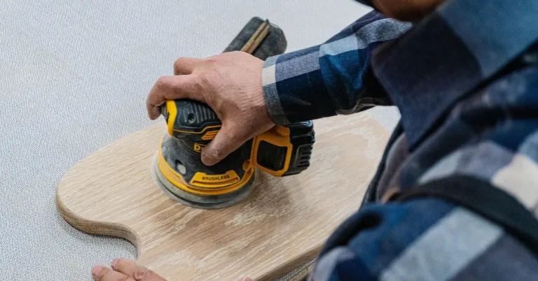 Cordless random orbital sander polishing a wood workpiece with its foam-backed pad