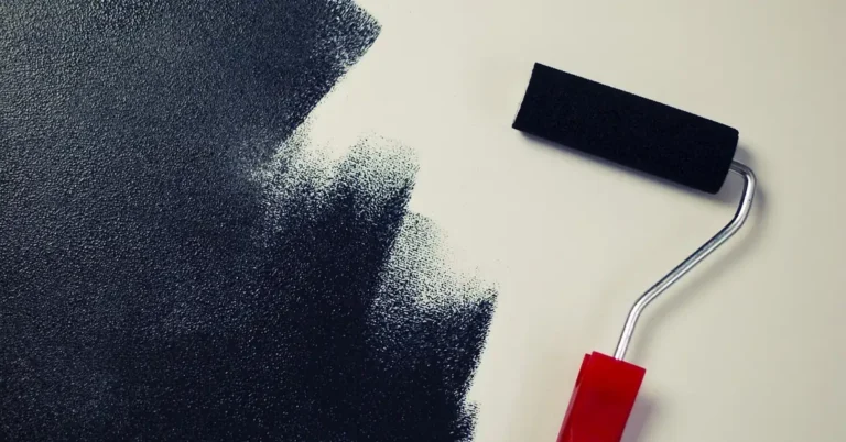 Paint roller with red handle rolling dark paint onto a light wall