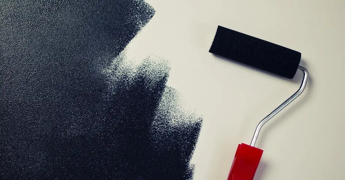 Paint roller with red handle rolling dark paint onto a light wall