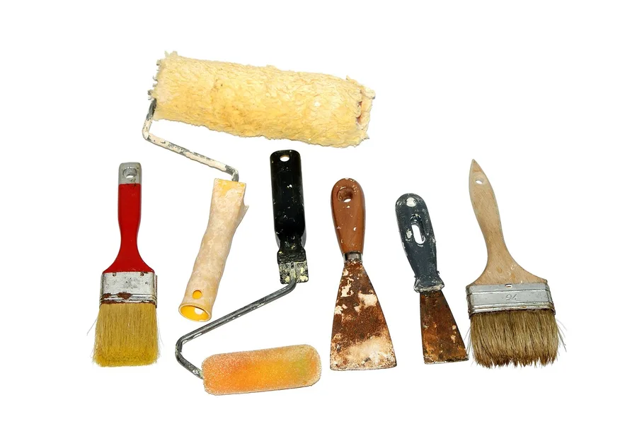 Paint rollers, brushes and scrapers laid out on a white background