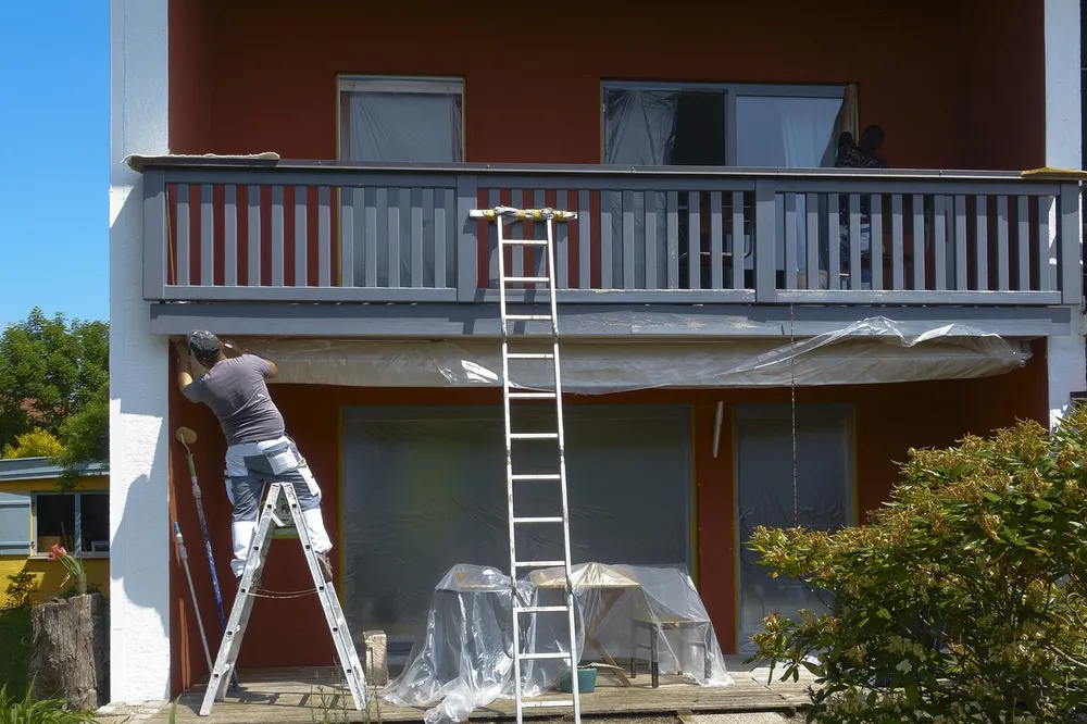 Painter on a ladder painting the exterior wall of a house without scaffolding
