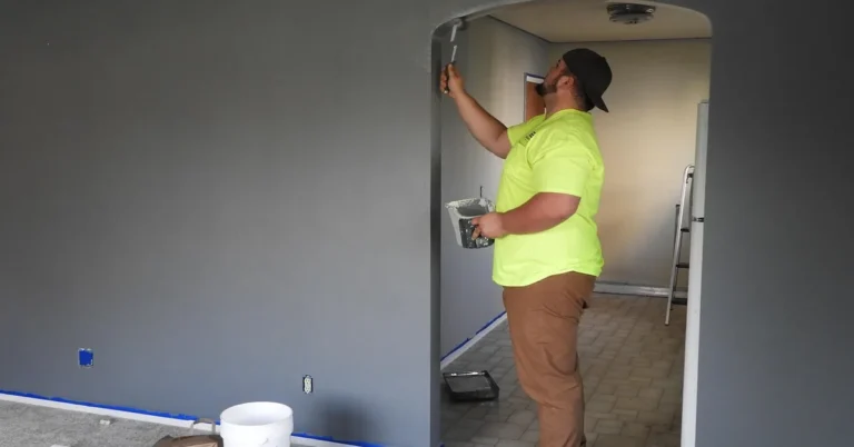 Professional painter using a brush to cut in gray latex wall paint near a doorway