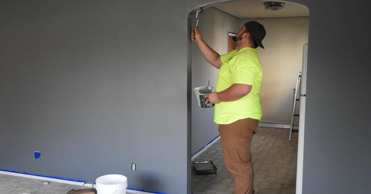 Professional painter using a brush to cut in gray latex wall paint near a doorway
