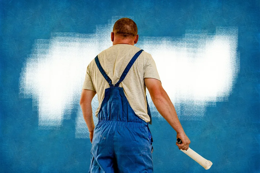 Painter rolling paint onto an exterior wall section without scaffolding