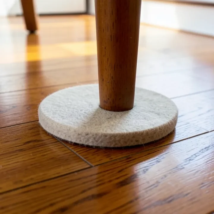 Round felt glide attached to the bottom of a wood chair leg on a hardwood floor