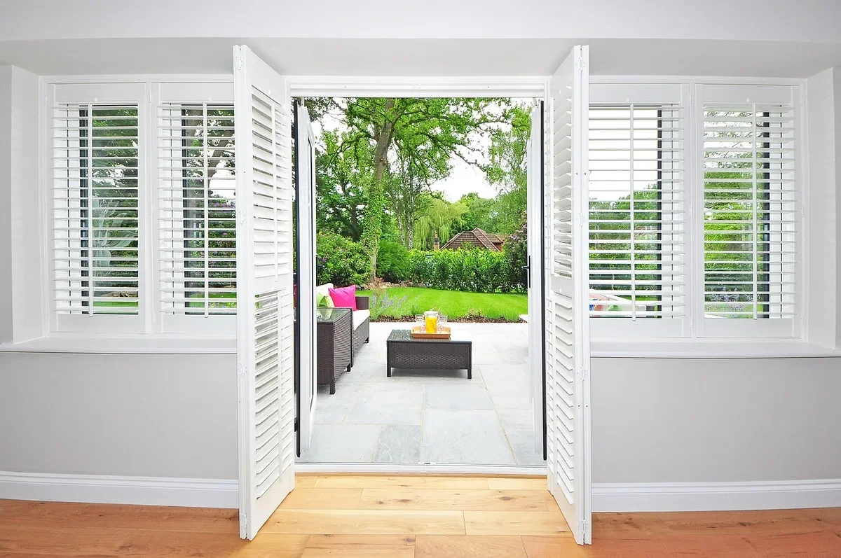 White interior plantation shutters folded open beside a set of patio doors