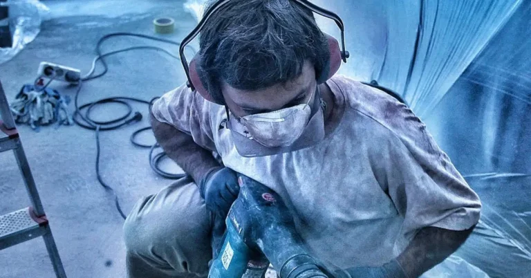 Worker in ear protection and dust mask using a corded hammer drill on a wall