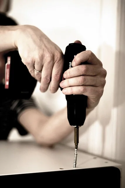 Hands using a cordless driver to drive a screw into a furniture panel