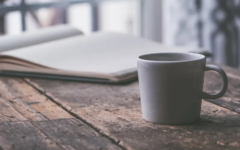 Grey mug set directly on a rustic wood tabletop beside an open notebook Grey mug set directly on a rustic wood tabletop beside an open notebook