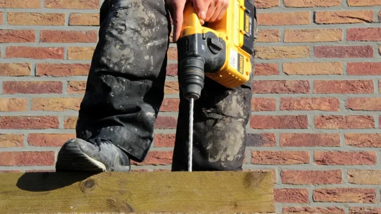 Worker holding a hammer drill with a masonry bit beside a wood plate on a brick wall ledge