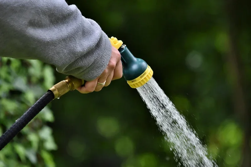 Hand holding a garden hose spray nozzle to rinse a fence from above Hand holding a garden hose spray nozzle to rinse a fence from above