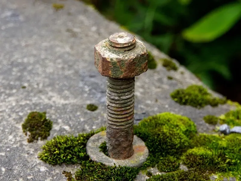 Corroded steel anchor bolt with washer set in a concrete slab with moss growing around it