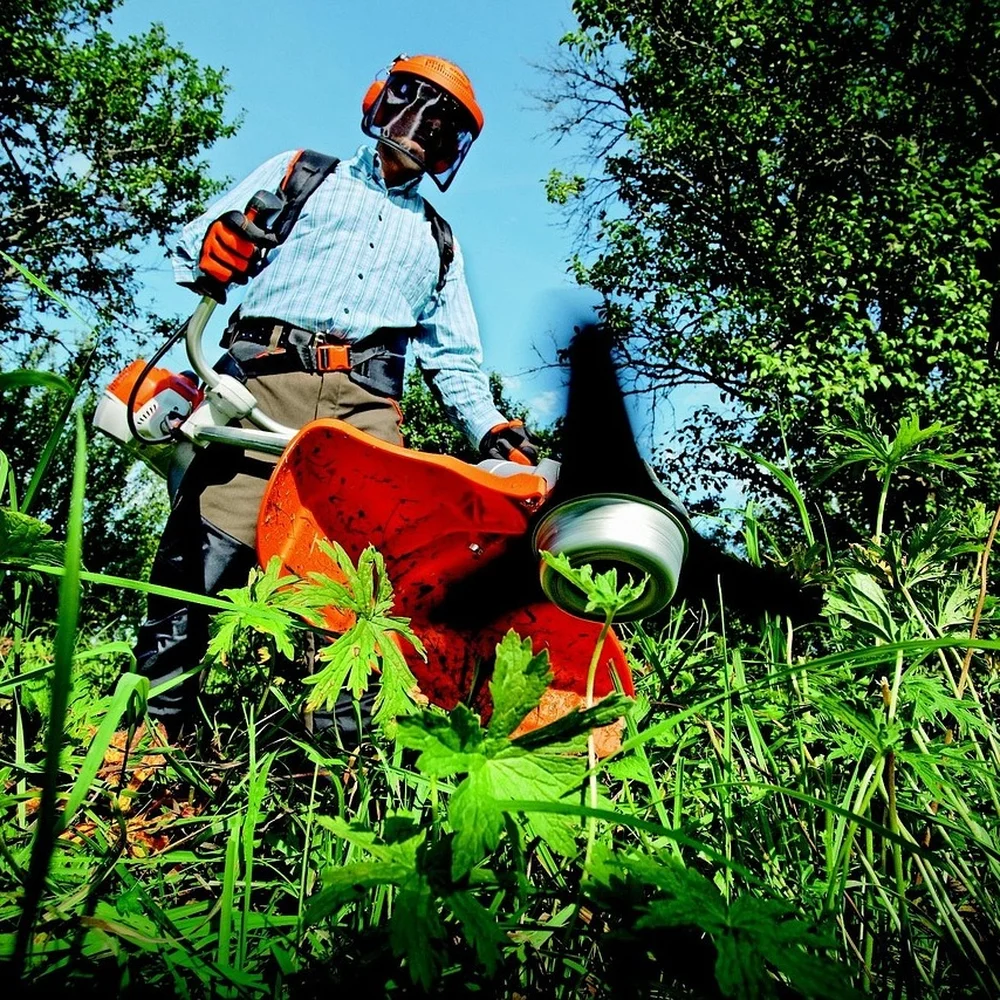 Landscaper using a KombiSystem-style powerhead attachment in dense vegetation