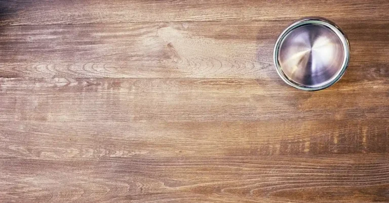 wood table surface with a faded water mark in the grain near a metal bowl