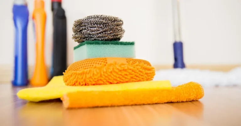 Microfiber cloths and sponges on a wood floor next to a baseboard for cleaning woodwork