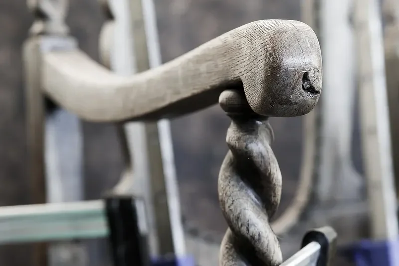 Stripped antique oak armchair arm and barley-twist post clamped in a restoration workshop
