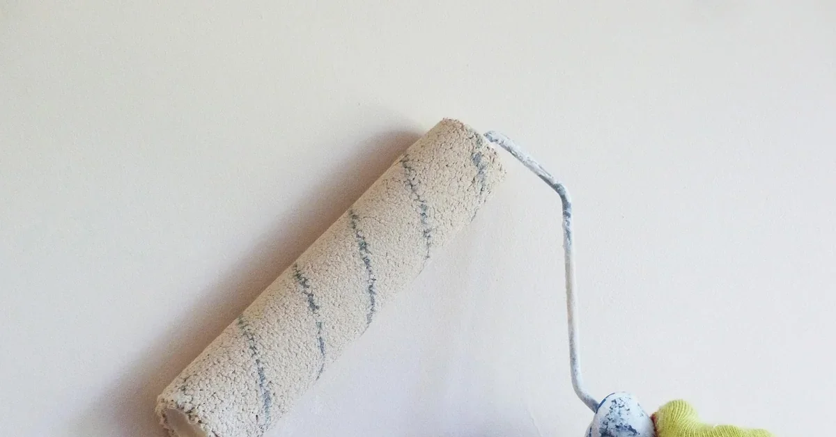 Paint roller rolling a coat of white paint onto an interior wall
