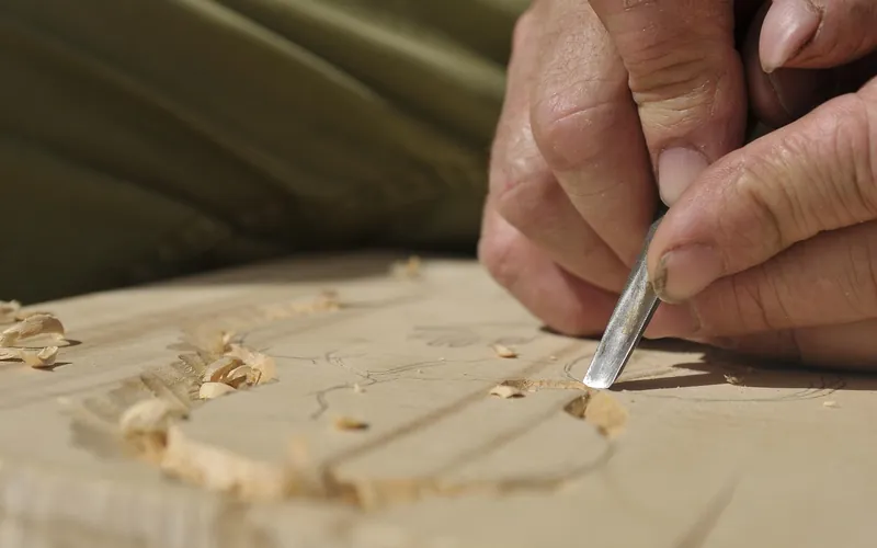 Hand using a carving chisel to lift shavings from a flat wood surface