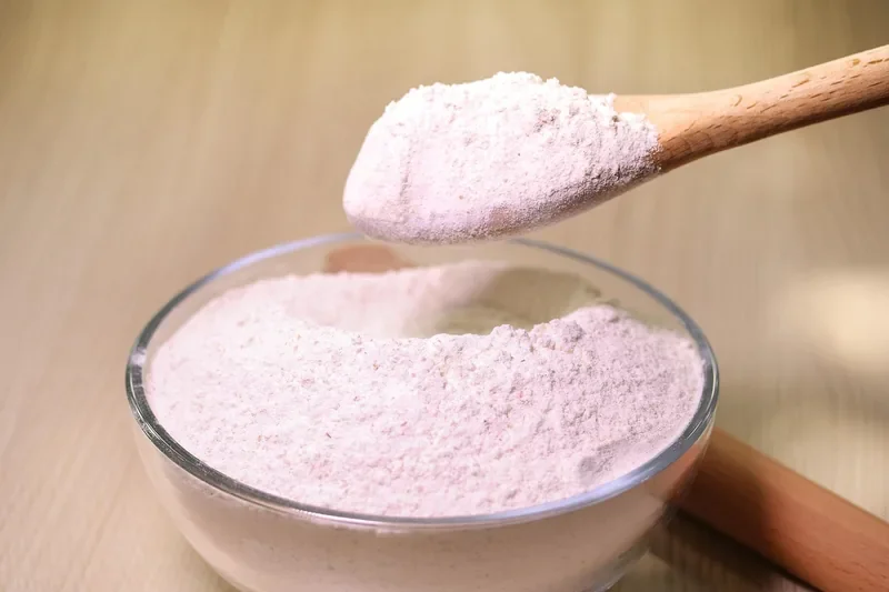 Plain flour in a glass bowl with a wooden spoon, the base ingredient for homemade flour paste