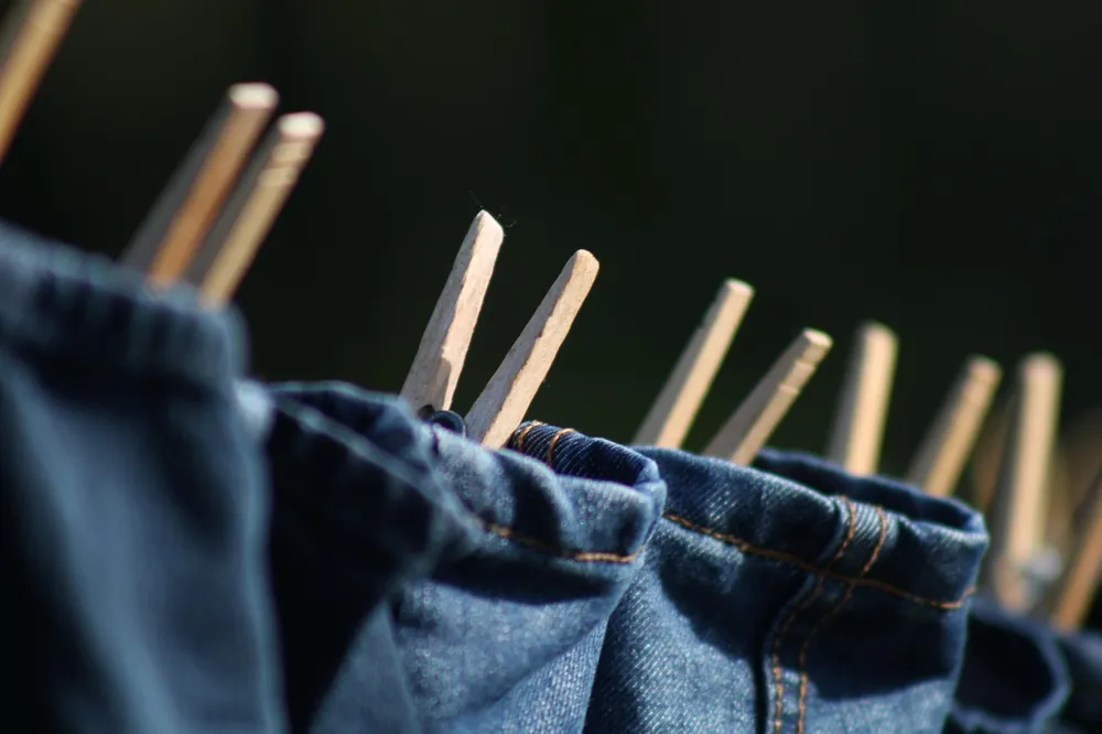 Blue jeans hanging on a clothesline with wooden pegs to air dry after glue stain treatment