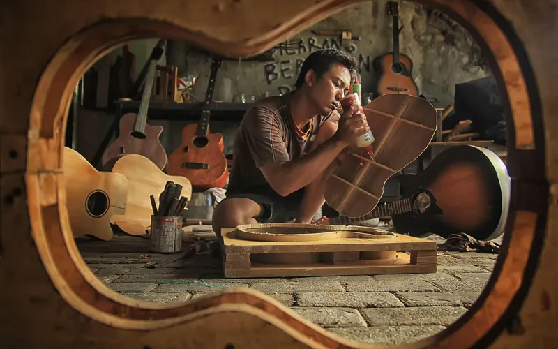 Luthier applying glue to a guitar top in a workshop