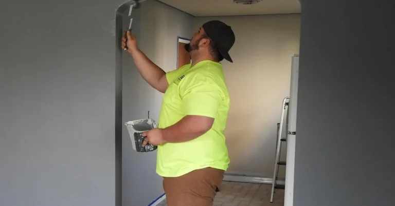 Blue painter's tape masking a baseboard and door trim while a room is being painted gray