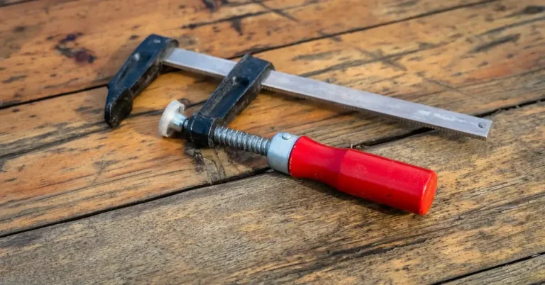 Steel bar clamp with red handle resting on a wooden workbench