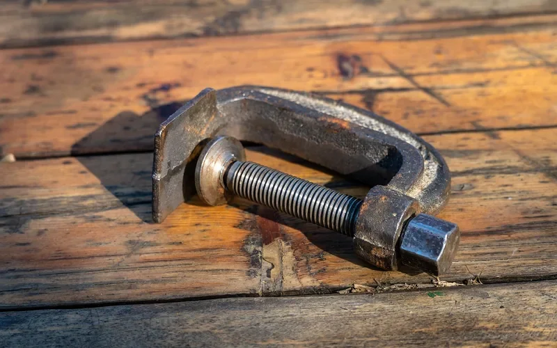 Steel C-clamp with a screw spindle on a wooden workbench Steel C-clamp with a screw spindle on a wooden workbench