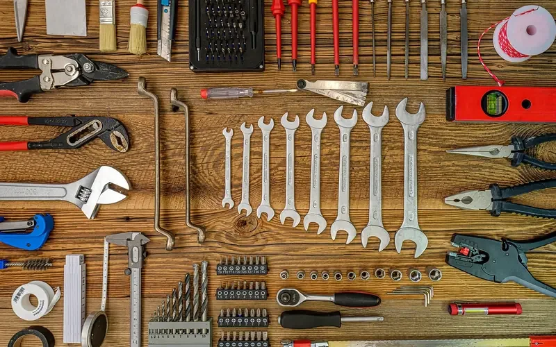 Flat lay of hand tools including a spirit level, drill bits and folding rule on a wood bench Flat lay of hand tools including a spirit level, drill bits and folding rule on a wood bench