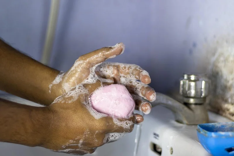 Hands lathering a bar of soap at a sink to wash off paint