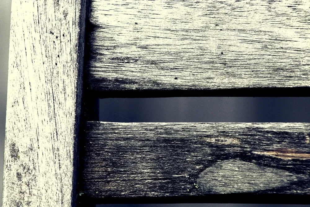 Close-up of weathered silver-gray teak chair slats with surface dirt and mildew spots