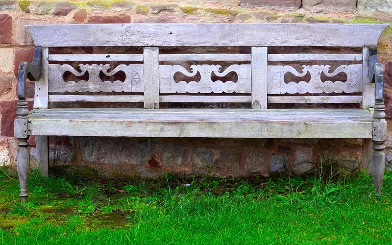 Weathered gray wooden garden bench against a stone wall