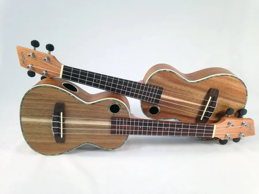 Two ukuleles made from golden-brown acacia wood with visible grain