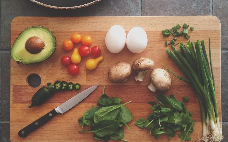 knife and fresh vegetables laid out on a wood cutting board in a kitchen