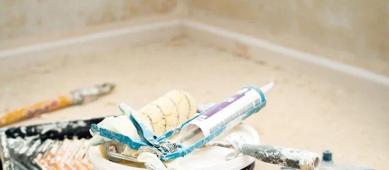 Caulk gun and paint roller resting on a bucket in a room being renovated