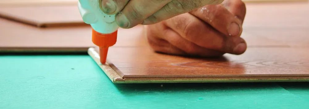 Applying glue to a plank edge over green foam underlayment on a floating floor