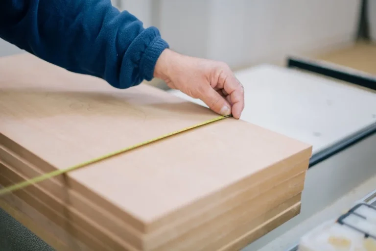 Hand holding a tape measure across a stack of MDF panels