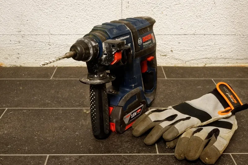Cordless rotary hammer with an SDS bit next to a pair of work gloves Cordless rotary hammer with an SDS bit next to a pair of work gloves