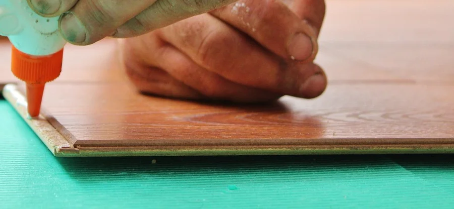 Hand applying wood glue from a bottle to the edge of a floorboard Hand applying wood glue from a bottle to the edge of a floorboard