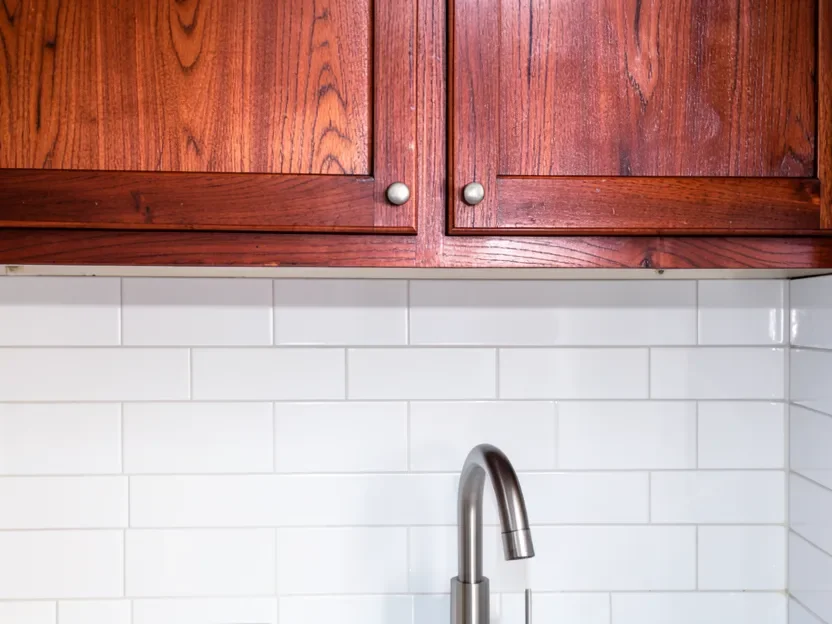 Close-up of deep reddish-brown cherry cabinets above a white subway tile backsplash