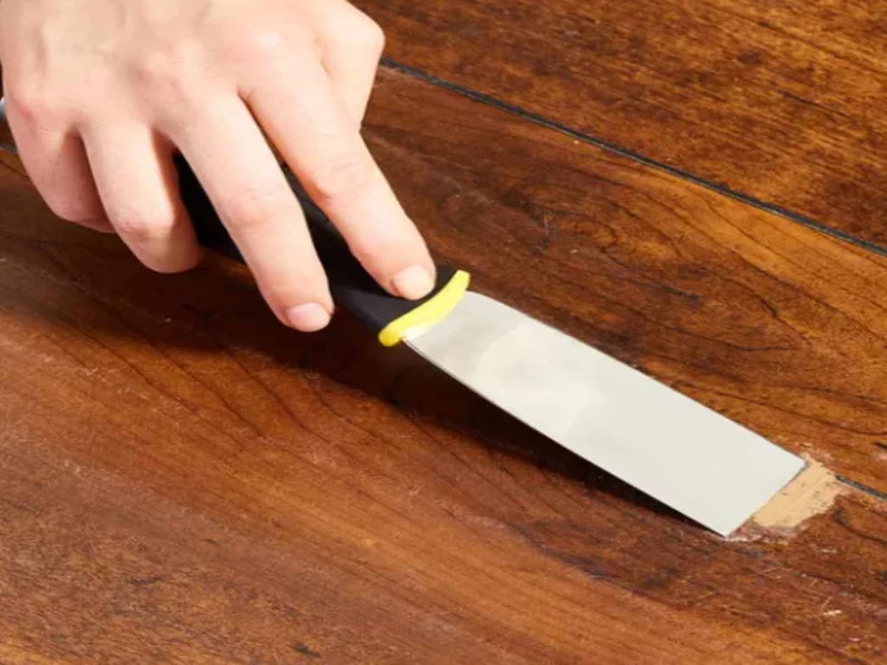 Pressing wood filler into a deep gouge with a plastic putty knife